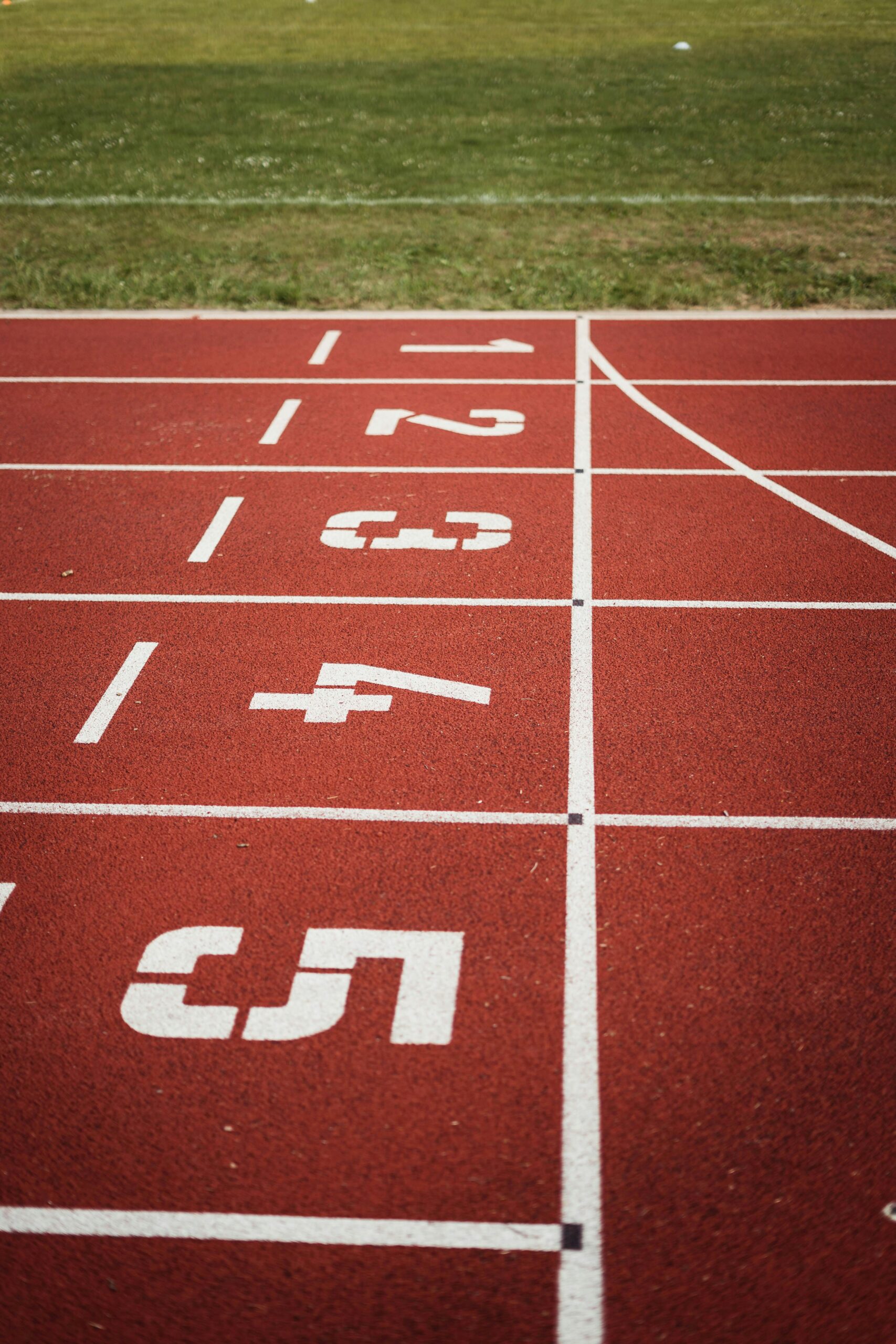 Home - english Close-up view of a red running track with numbered starting lanes, perfect for athletic themes.